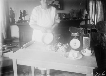 Woman making an apple charlotte cake using a marble slab for rolling the pastry, sliced apples, scales, grater, lard and butter for pastry.