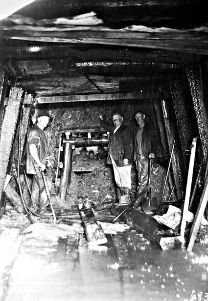 Three miners underground working on sewerage tunnel which has just broken through to another tunnel.See the men in the background