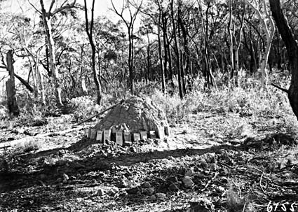 Mound in the bush surrounded by plaques with a mattock on top